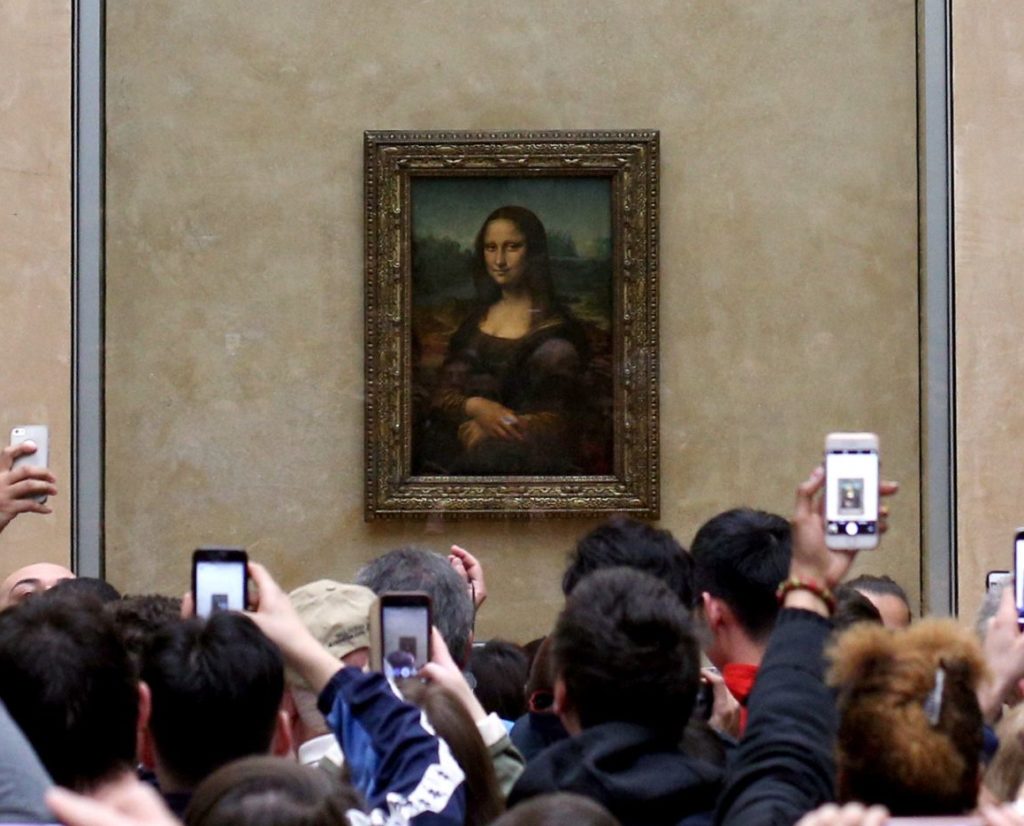 Museum visitor photo of the Mona Lisa painting surrounded by people.